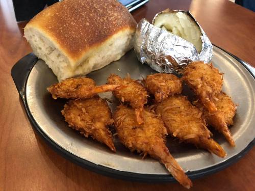 A plate with crispy coconut shrimp, a baked potato wrapped in foil, and a piece of bread.