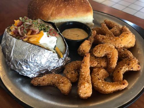 A plate featuring a baked potato with toppings, a roll, and crispy fried shrimp with a dipping sauce.
