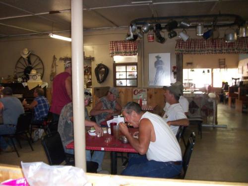 A casual diner scene with men eating and chatting at tables, surrounded by rustic decor and kitchen items.