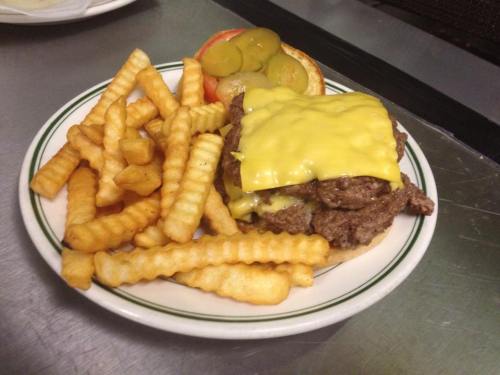 A plate with a cheeseburger topped with melted cheese, pickles, and tomato, served with crinkle-cut fries.