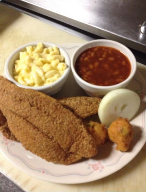A plate with fried fish, macaroni and cheese, baked beans, and a slice of onion.