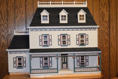 A detailed model of a Victorian-style house with multiple windows and a porch, set against a wooden background.