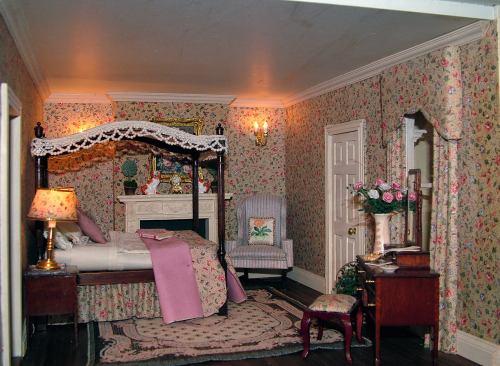 A cozy, vintage-style bedroom with floral wallpaper, a four-poster bed, and elegant furnishings.