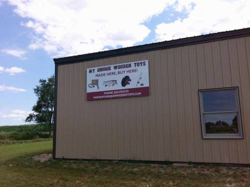 Sign on a building promoting "My Unique Wooden Toys" with contact information and a message to buy locally.