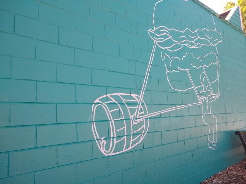 A mural on a teal wall depicting a person pushing a large burger on a wheel.