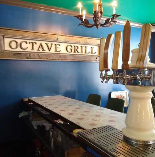 Interior of Octave Grill featuring a bar with beer taps and a blue wall, illuminated by a chandelier.