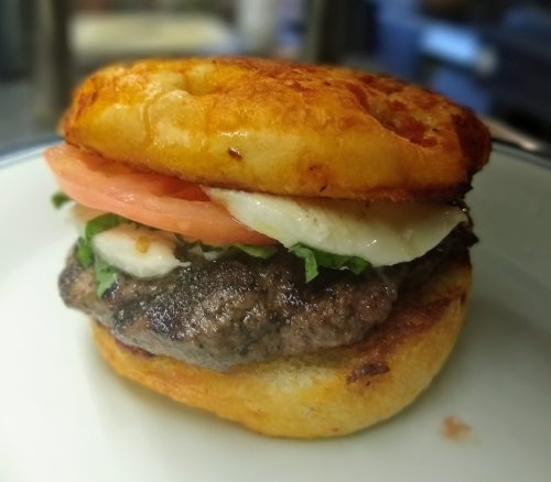 A close-up of a juicy burger with lettuce, tomato, and cheese on a toasted bun, served on a white plate.