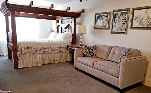 Cozy bedroom with a four-poster bed, a beige sofa, and framed artwork on the wall. Soft lighting creates a warm atmosphere.
