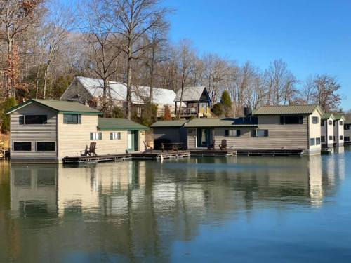 A serene lakeside scene featuring houseboats with green roofs, surrounded by trees and clear blue skies.