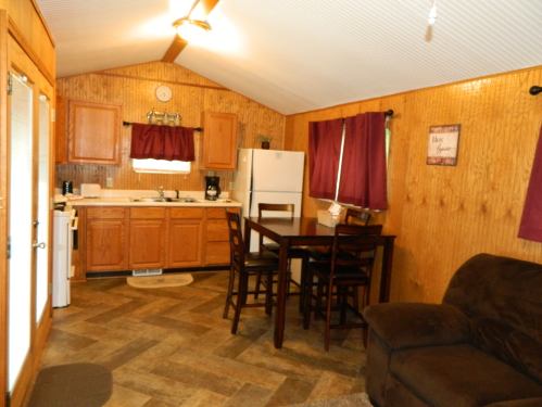 Cozy kitchen with wooden cabinets, a dining table, and a living area featuring a brown couch and warm decor.