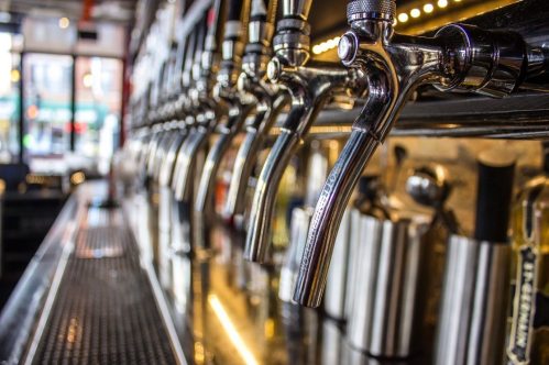 Close-up of shiny beer taps lined up at a bar, with a blurred background of the bar setting.