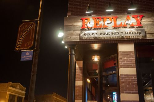Sign for "Replay" restaurant featuring beer, bourbon, and dining, with a street sign for Andersonville in the background.