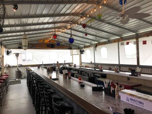 A spacious outdoor bar area with a long counter, colorful decorations, and fans under a metal roof.
