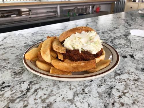 A plate with a fried chicken sandwich topped with coleslaw, served alongside golden French fries on a marble countertop.