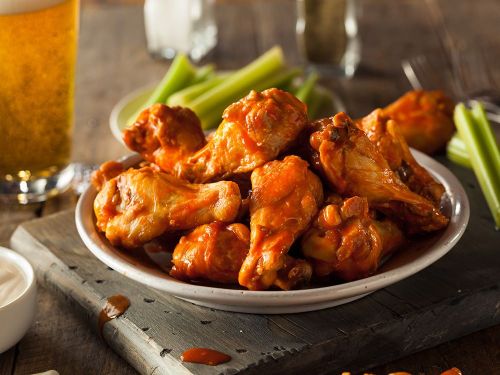 A plate of spicy chicken wings with celery sticks, accompanied by a glass of beer on a wooden table.