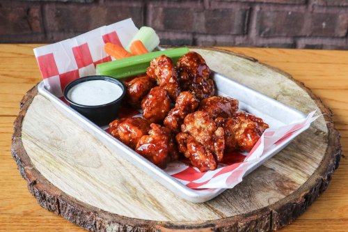 A platter of saucy chicken wings with celery, carrots, and a side of ranch dressing on a wooden serving board.