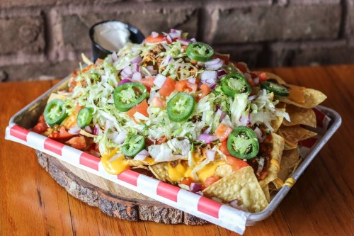 A large platter of nachos topped with cheese, lettuce, tomatoes, jalapeños, onions, and a side of sour cream.