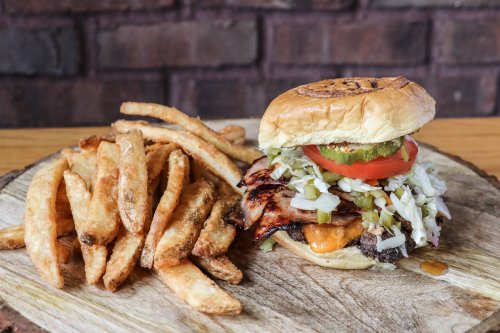 A juicy burger with lettuce, tomato, pickles, and cheese, served with a side of crispy fries on a wooden platter.