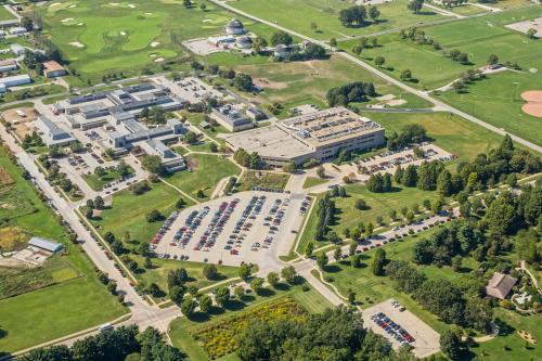Aerial view of a large campus with multiple buildings, parking lots, and green spaces, surrounded by golf courses.
