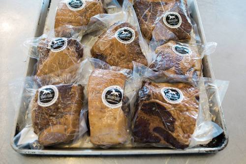 A tray of vacuum-sealed meat packages, each labeled with a logo, arranged neatly on a metal surface.