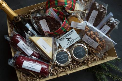 A gift basket filled with gourmet foods, including cheese, mustard, honey, snacks, and a bottle of sparkling wine.