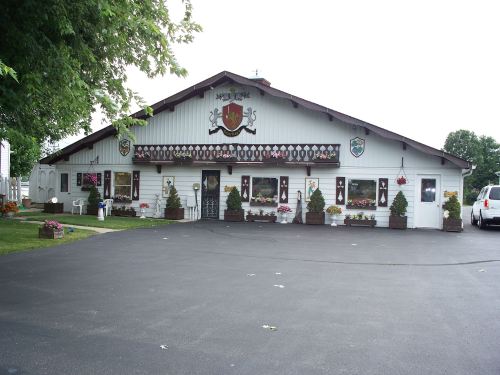 A large, decorative building with flower beds, featuring a crest and various wall decorations, set in a green landscape.