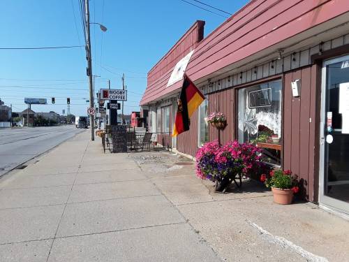 A street view of a small shop with a German flag, colorful flowers, and a Biggby Coffee sign on a sunny day.