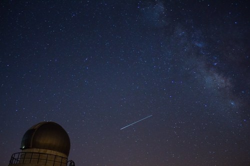 A starry night sky with the Milky Way and a meteor streaking above a dome-shaped observatory.