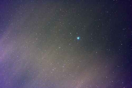 A night sky filled with stars, featuring a bright celestial object among a backdrop of faint stars and clouds.