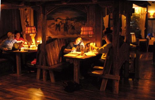 Cozy restaurant interior with dim lighting, wooden booths, and patrons engaged in conversation and dining.