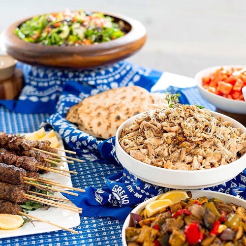 A vibrant spread of Mediterranean dishes, including skewers, shredded chicken, salad, and pita bread on a blue tablecloth.
