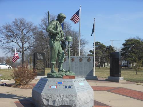 A soldier statue stands on a pedestal, surrounded by flags and memorials honoring military service.