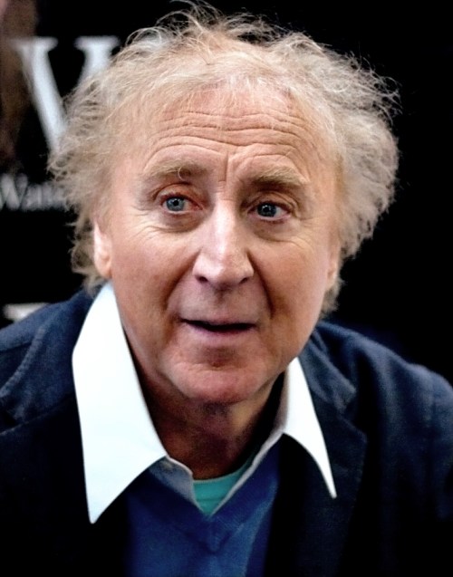 A middle-aged man with curly hair and blue eyes, wearing a blue sweater and white collared shirt, smiling.