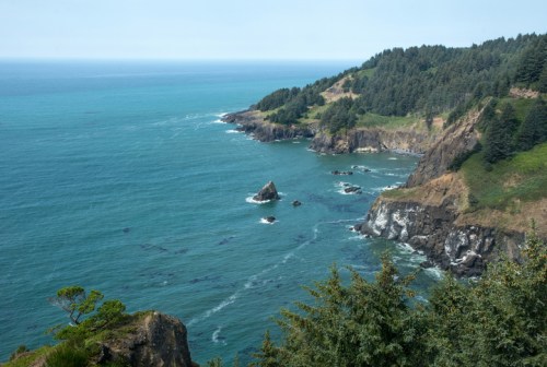 A scenic coastal view featuring rocky cliffs, turquoise waters, and lush greenery along the shoreline.