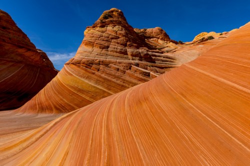Vibrant orange and yellow rock formations with swirling patterns under a clear blue sky.