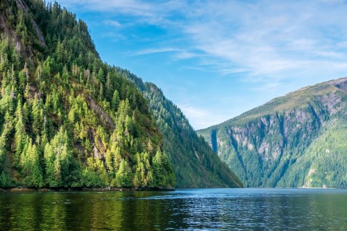 Lush green mountains rise above a calm, reflective body of water under a clear blue sky.
