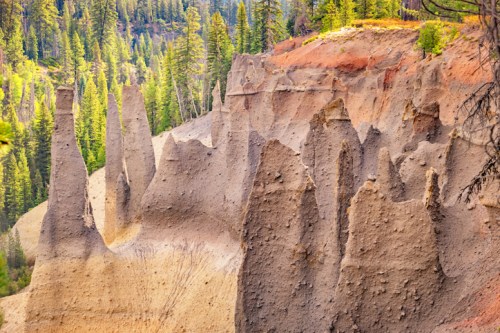 Rock formations rise sharply from the ground, surrounded by lush green trees in a vibrant natural landscape.