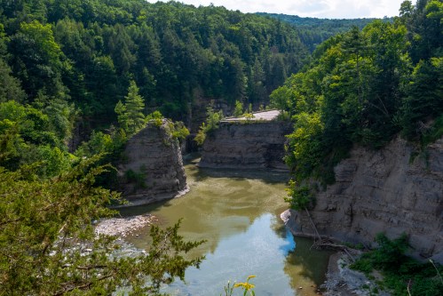 A serene river winding through lush green cliffs and trees under a clear blue sky.