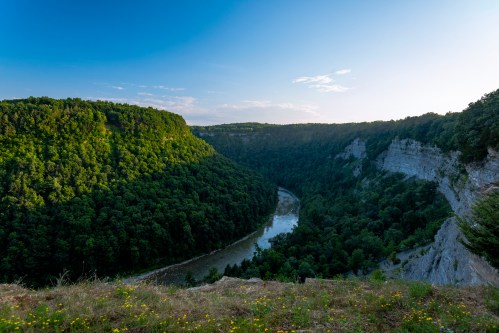 A scenic view of a lush green valley with a winding river, surrounded by steep cliffs under a clear blue sky.