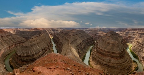 A panoramic view of a winding river surrounded by steep, layered canyon walls under a cloudy sky.