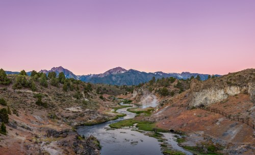 A serene landscape featuring a winding river, mountains, and a pastel sky at dusk.