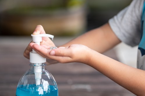 A person pumps blue liquid soap into their hand from a plastic bottle.