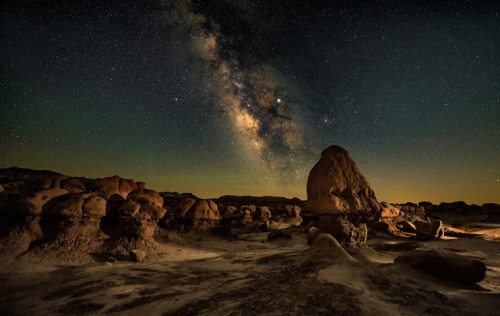 A starry night sky with the Milky Way over unique rock formations in a desert landscape.