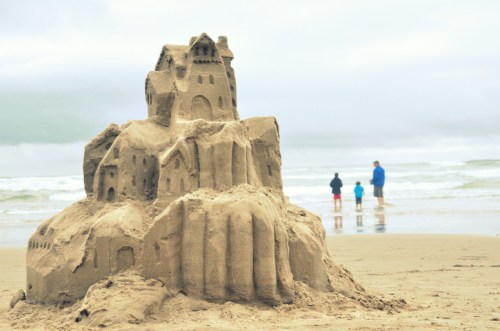A detailed sandcastle on the beach, with a family in the background walking along the shore.