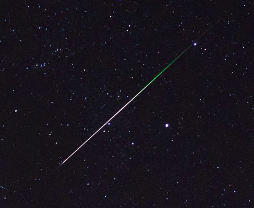 A bright meteor streaks across a starry night sky, leaving a glowing trail behind it.