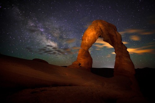 A night sky filled with stars above a sandstone arch, illuminated by soft light, creating a serene landscape.
