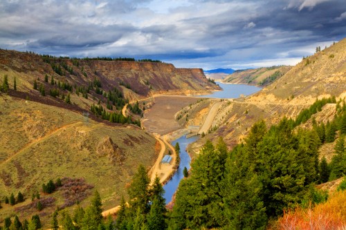A scenic view of a winding river surrounded by rugged hills and trees under a cloudy sky.