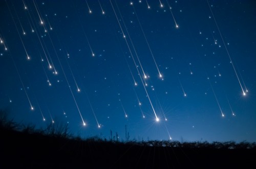 A night sky filled with streaking stars, creating a dynamic display against a dark horizon.