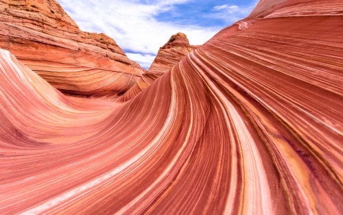 Colorful, undulating rock formations with layered stripes in a desert landscape under a blue sky.