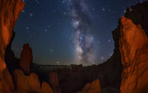 A stunning night sky filled with stars and the Milky Way, framed by rocky formations in a dark landscape.